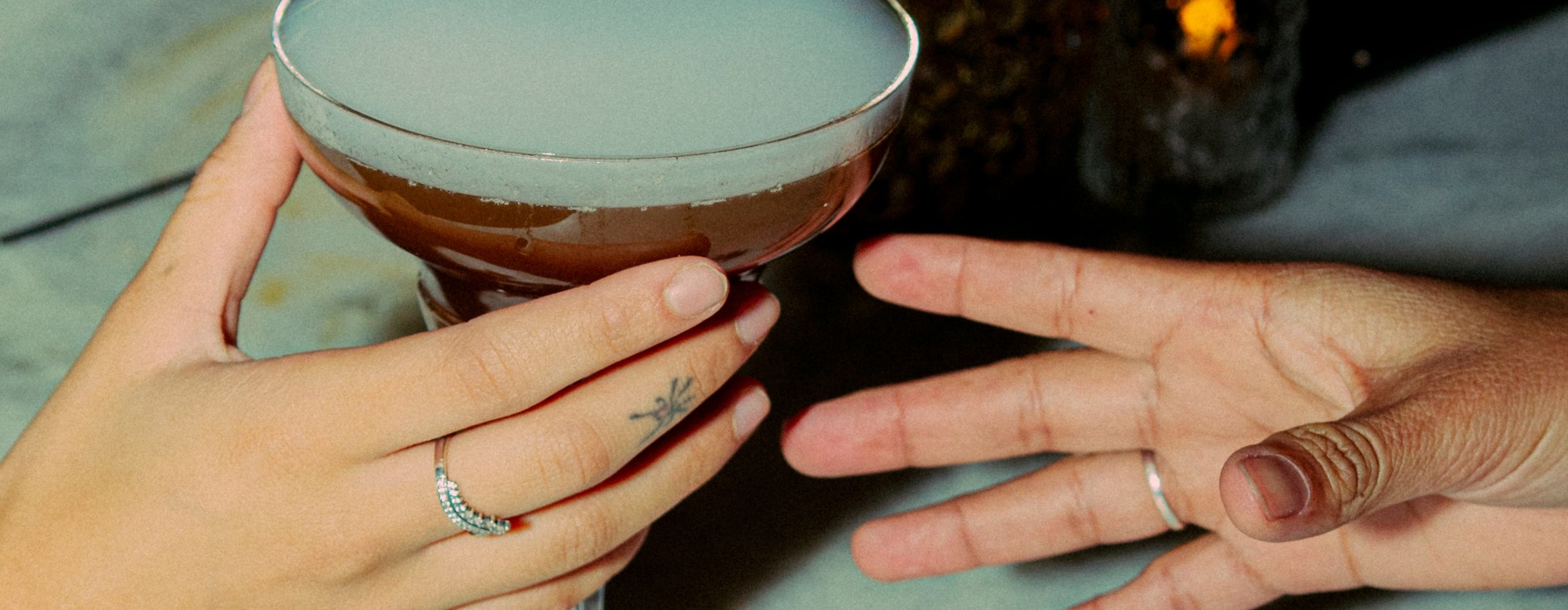 hands sharing a cocktail indoors