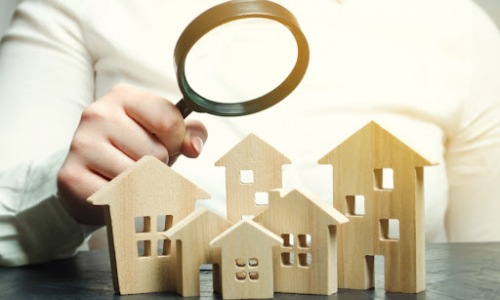 person holding microscope over small wooden residential buildings